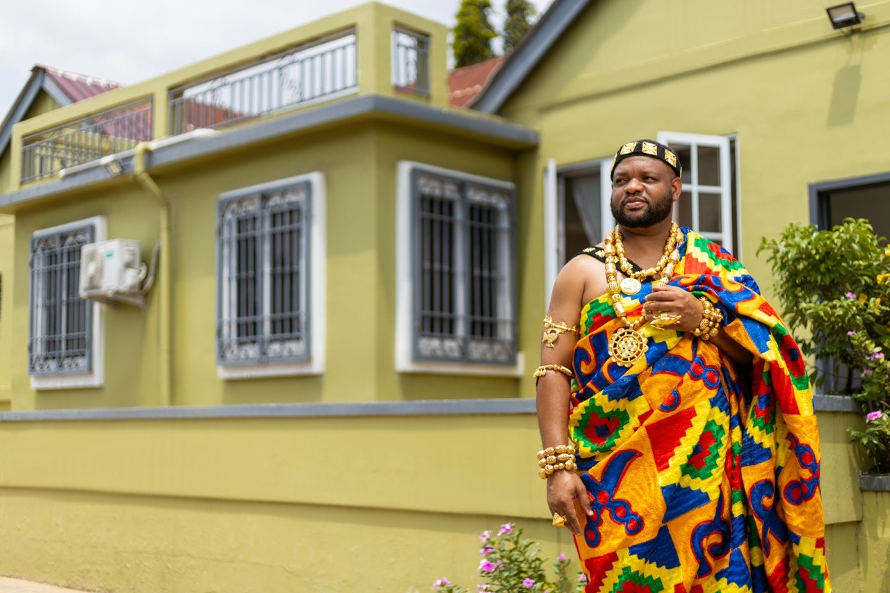 Edward outdoors in colourful kente and gold regalia